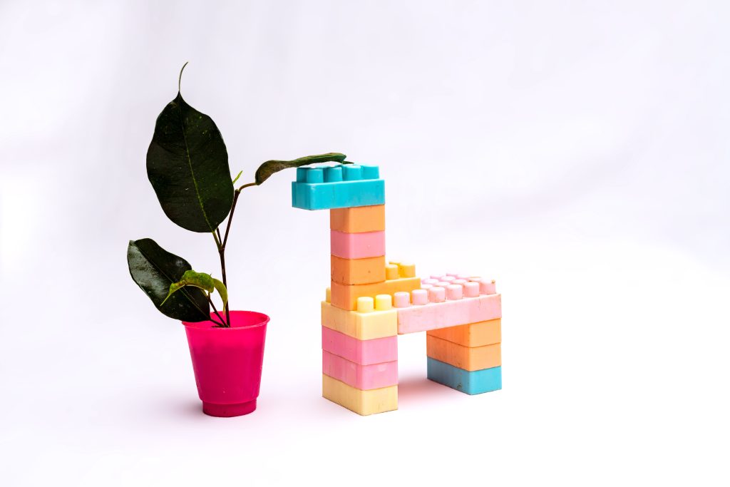 A digital photograph of a lego Giraffe eating a plant; a material metaphor to represent development as the giraffe always eating the fresh leaves at the top, leaving those at the bottom to wither.